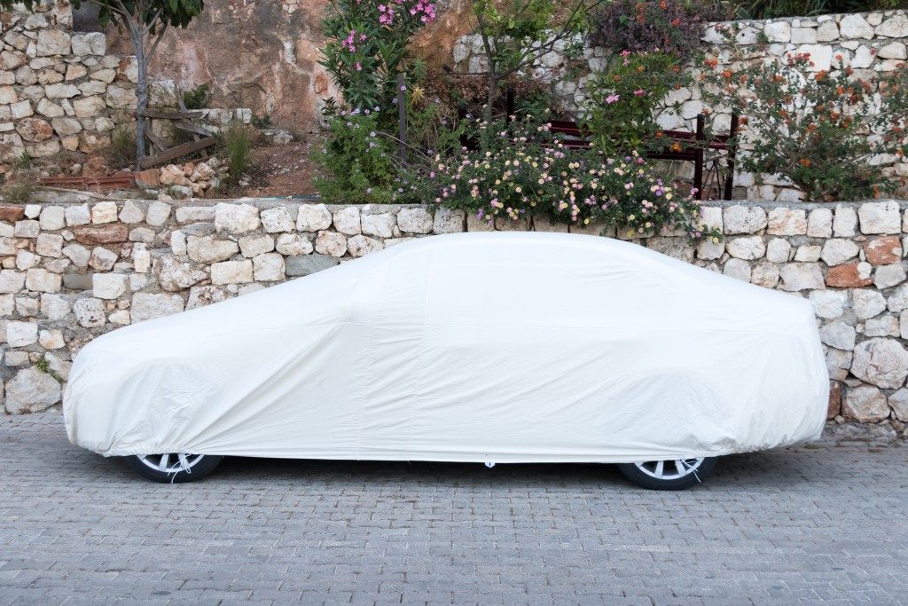 Car covered with white sheet on the pavement
