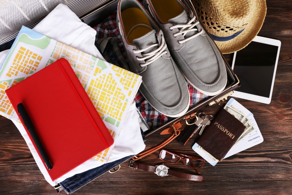 Packed suitcase of vacation items on wooden table, top view