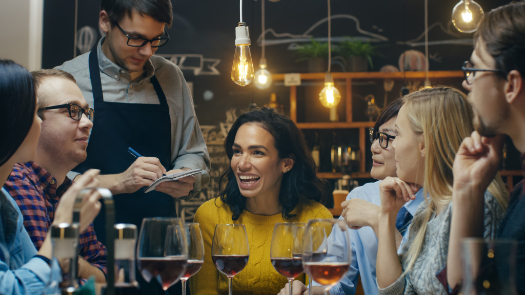 A group of friends happily drinking wine while a waiter is taking their orders