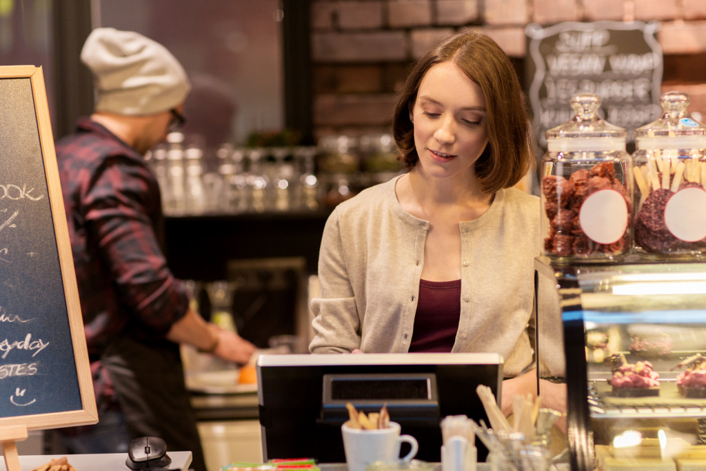 Woman or bartender at cafe or coffee shop counter with cashbox
