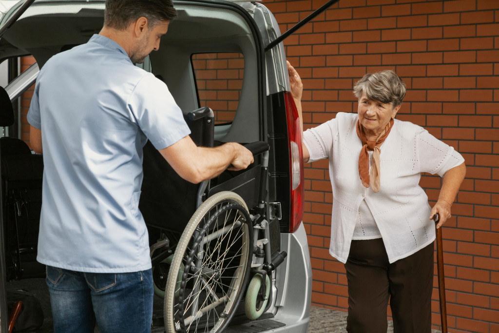 A concerned man helping an elderly neighbor mount her wheelchair in a van