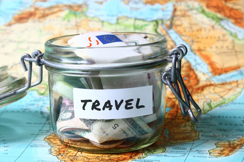 A glass container with money labeled Travel on a world map