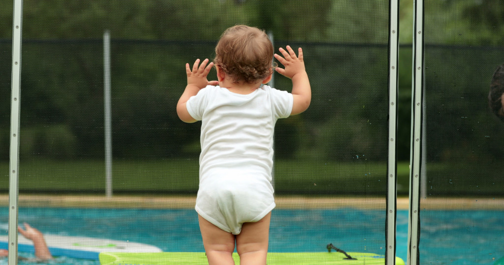 A baby leaning on a pool fence