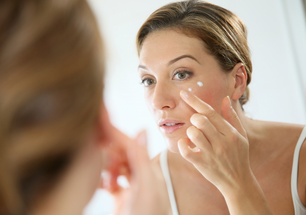 woman adding face cream in her cheeks while looking in a mirror